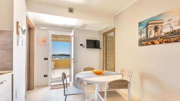 A dining area with a table and chairs, a painting of the Arc de Triomphe, and a view through an open door to a balcony. - 2206 Perla del Boncore (Nardò)