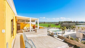 A yellow building with a terrace, outdoor seating, and a view of a green landscape. - 2206 Perla del Boncore (Nardò)
