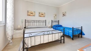 A bedroom with a single bed, a nightstand, and a small table. There are three wall-mounted paintings and a window with a curtain. - 2206 Perla del Boncore (Nardò)