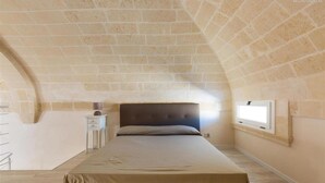 Ein Schlafzimmer mit gewölbter Decke, einem Bett, einem Nachttisch und einem Fenster.