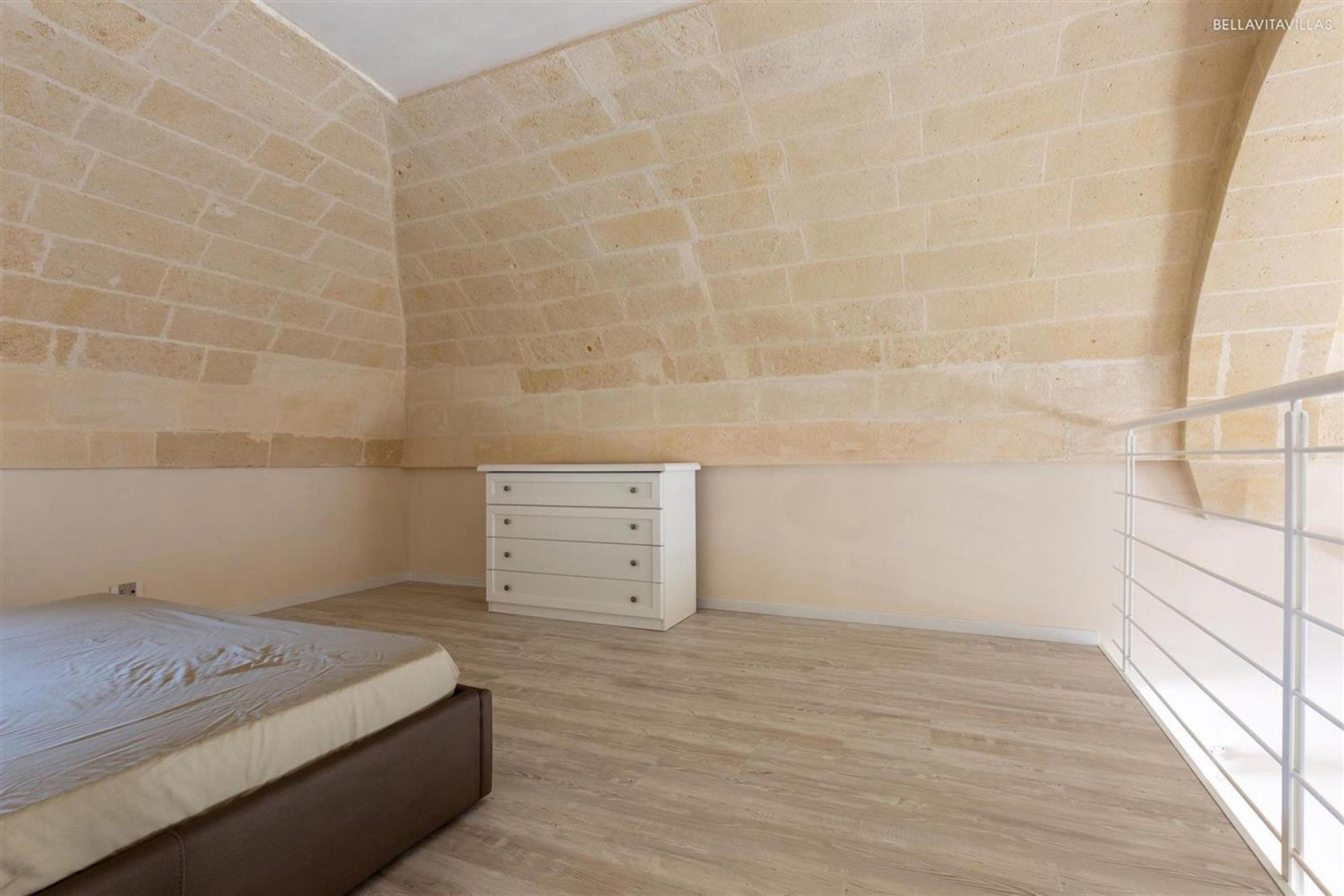 A room with a bed, a dresser, and a brick wall.