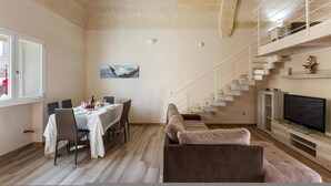 Ein Essbereich mit Tisch für vier Personen, eine Treppe und ein Wohnzimmer mit Sofa und Fernseher.