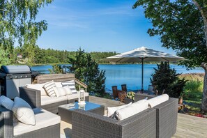 An outdoor deck with wicker furniture, a grill, and a view of a lake. - Gorgeous Villa Funkis Strömmen by Sea (Pargas)