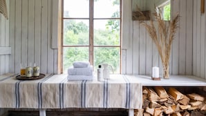 Une chambre rustique avec une grande fenêtre, une table en bois sur laquelle sont posées des serviettes et des articles de toilette, et une pile de bois de chauffage.