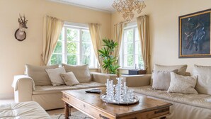 Un salon avec un canapé beige, une table basse en bois sur laquelle est posée une barrette de bougies, et une tête de cerf fixée au mur.