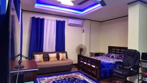 Un dormitorio con una cama, un escritorio, una silla y un ventilador.