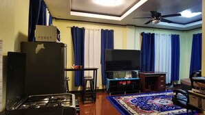 Un espacio habitable compacto con ventilador de techo, televisor de pantalla plana, refrigerador, estufa a gas y una alfombra estampada.