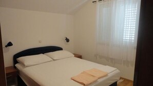 Ein Einzelbett mit weißer Bettwäsche und einer beigen Decke, ein Nachttisch und eine Wandlampe.