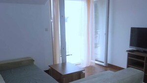 Ein kleiner, einfach eingerichteter Raum mit einem Bett, einem Fernseher und einer Glastür zum Außenbereich.