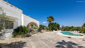 A courtyard with a swimming pool, palm trees, and a white building with an archway. - 373 Villa con Piscina a Casarano Gallipoli (Casarano)