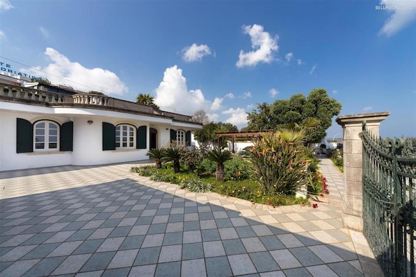 A courtyard with a tiled floor, a white building with green shutters, and a green fence.