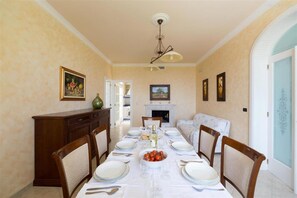 A dining room with a long table set for six, a fireplace, and a sofa.