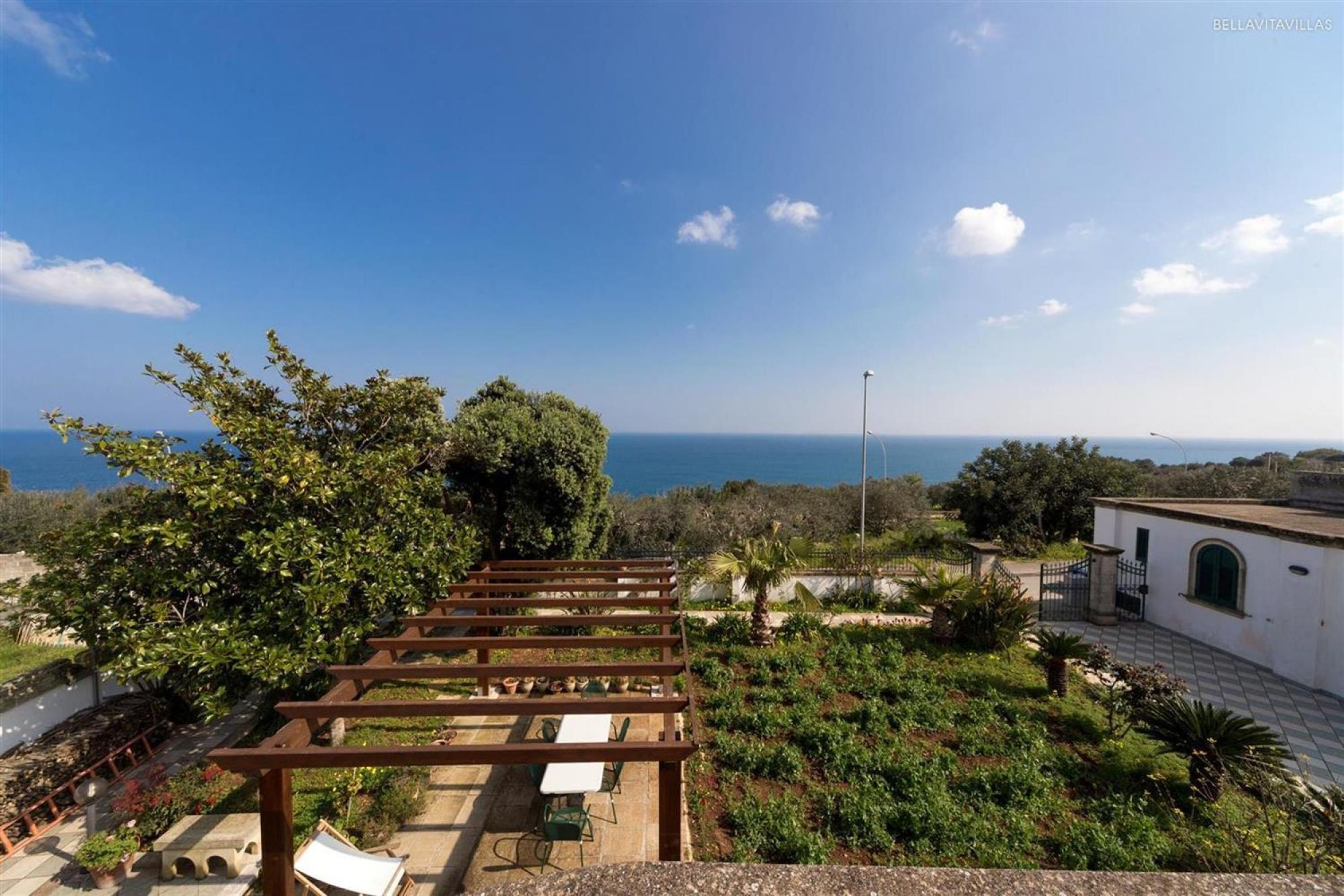 A rooftop garden with a pergola, seating area, and a view of the sea.