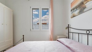 Un dormitorio con cama, armario, ventana con vistas y un cuadro en la pared.