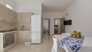 Una cocina moderna con armarios de madera clara, un refrigerador blanco y un comedor con mesa y sillas.