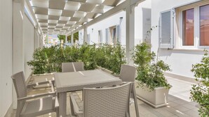 Un patio al aire libre con una mesa y sillas, rodeado de macetas con plantas y una estructura de pérgola.
