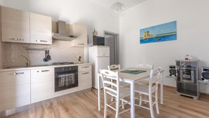 A modern kitchen with white cabinets, a gas stove, oven, and a dining area with a table and chairs. - 1183 Villino Delle Orchidee Est (Nardò)
