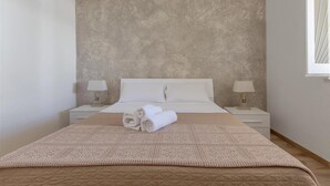 A neatly made bed with a patterned bedspread and pillows, two bedside tables with lamps, and a textured wall behind the bed. - 1183 Villino Delle Orchidee Est (Nardò)