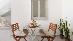 A dining area with a white table and two wooden chairs, a window above, and two potted plants on the floor. - 1432 Trilo Stella Di Mare 2 (Porto Cesareo)