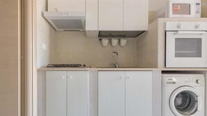 A compact kitchen with a microwave, oven, and washing machine. - 1542 Villetta Playa De Mar (Manduria)