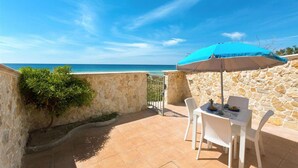 A patio with a stone wall, a table with chairs, and a blue umbrella. - 1542 Villetta Playa De Mar (Manduria)