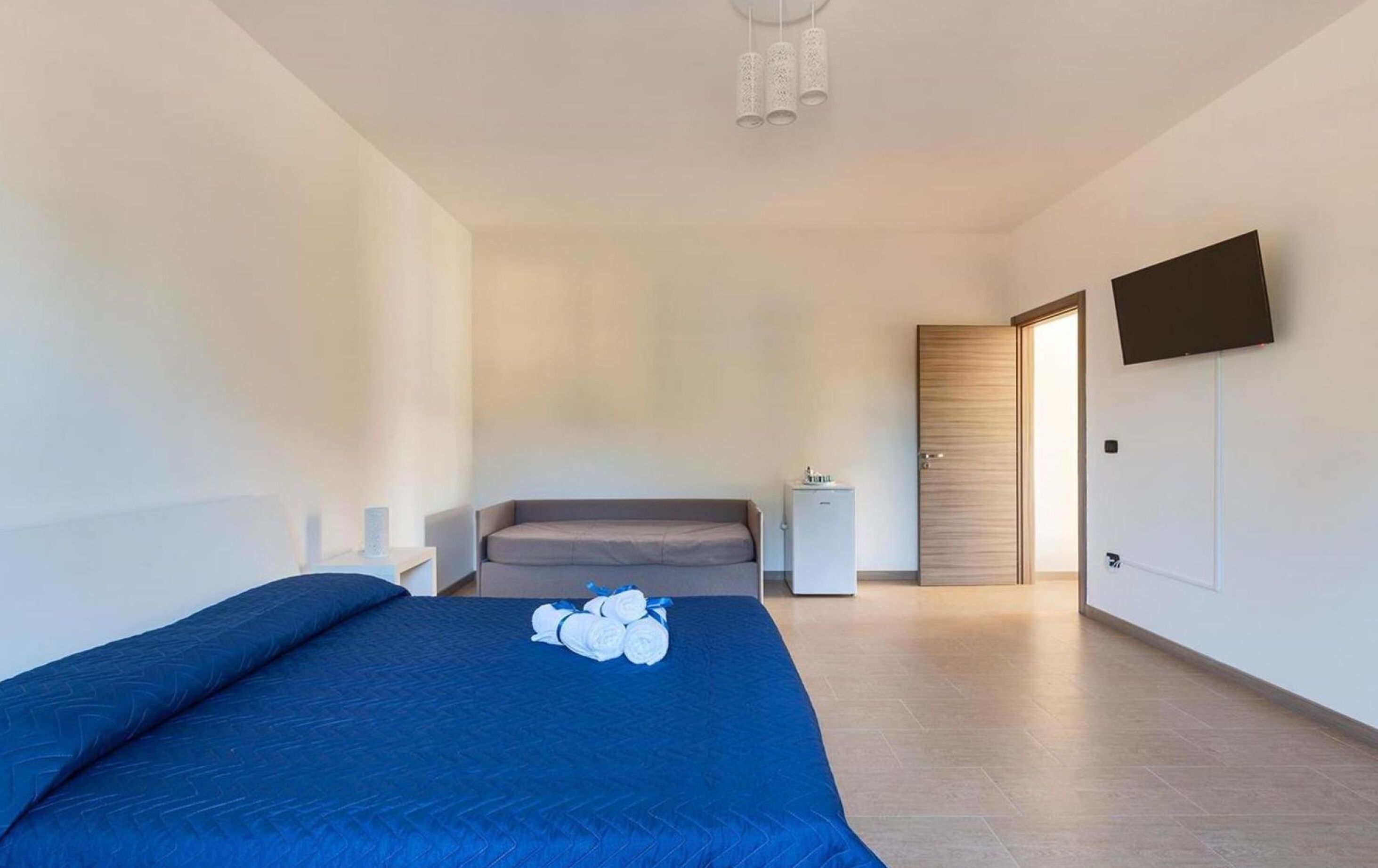 Ein Schlafzimmer mit einem Bett, einem Nachttisch, einer Kommode, einem Fernseher und einer Tür zu einem anderen Raum.