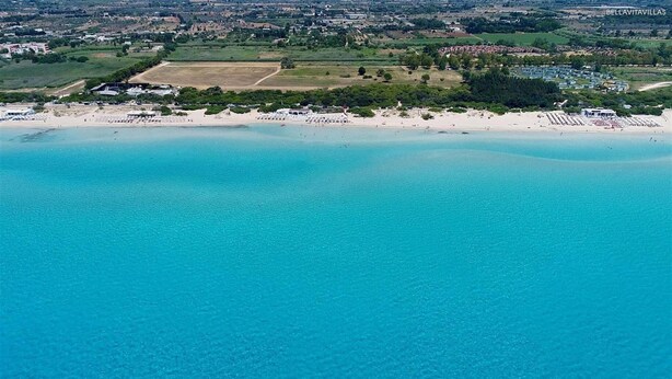 Luftaufnahme einer Küstenlandschaft mit Strand, Sportplatz und Wohngebäuden.