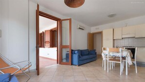 Ein Wohnzimmer mit Sofa, einem Esstisch mit Stühlen, einer Küchenzeile und einer offenen Tür zu einem anderen Raum.