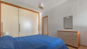 Ein Schlafzimmer mit einem Bett mit blauer Bettwäsche, einem Holzschrank, einer Kommode und einem Spiegel an der Wand.