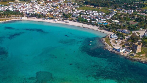 Luftaufnahme einer Küstenstadt mit Strand, Häusern und einem Turm.