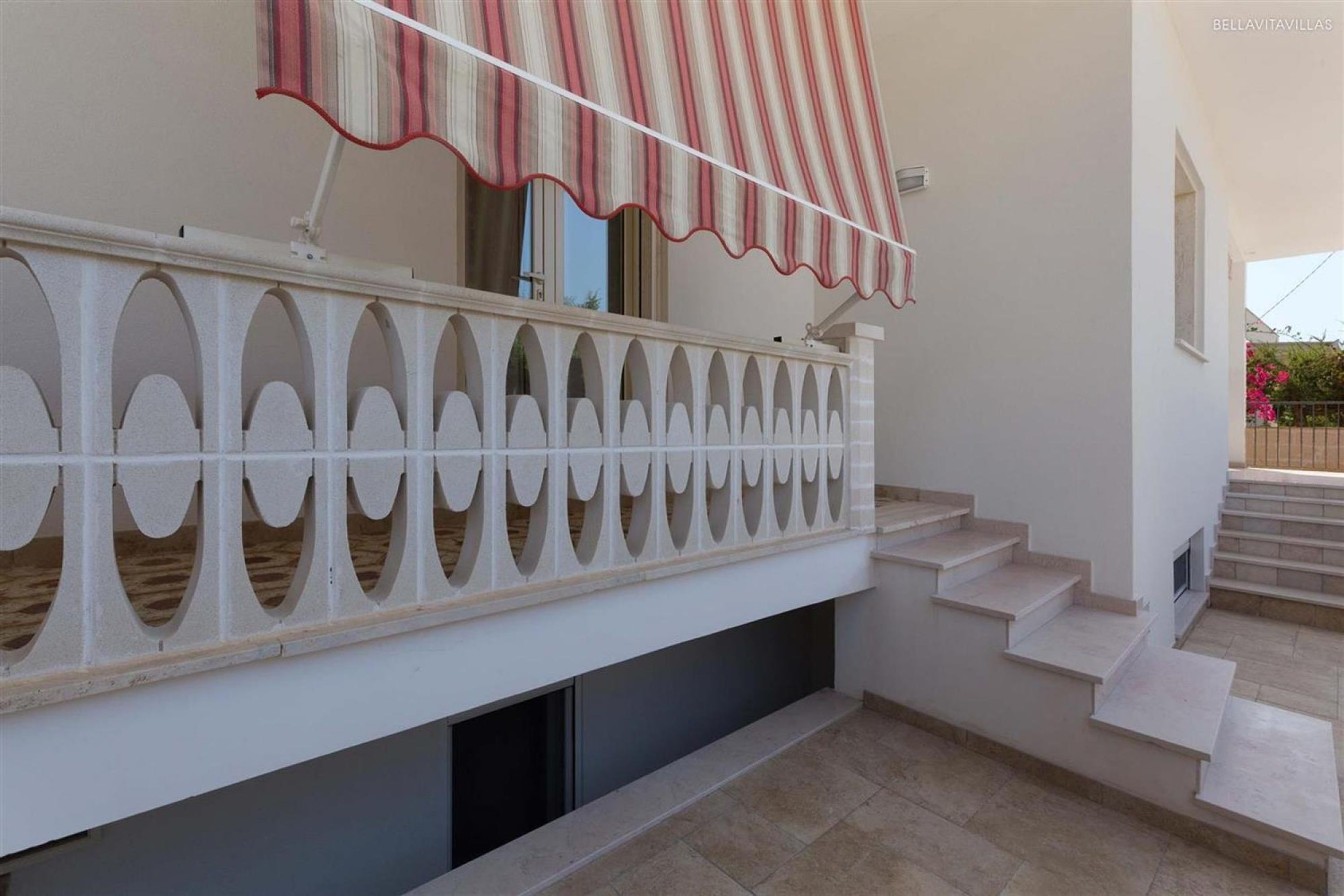 A white building with a balcony featuring a striped awning, a staircase, and a tiled floor.