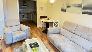 A living room with a sofa, a coffee table with a remote control, and a dining area with a table and chairs. - Beautiful 1-bed Apartment in Wimbledon- London (London)