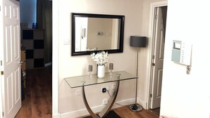 A hallway with a glass console table, a mirror, and a wall-mounted light fixture. - Beautiful 1-bed Apartment in Wimbledon- London (London)