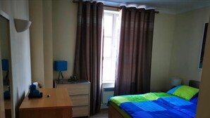 A bedroom with a bed, a dresser, a desk, and a window with curtains. - Beautiful 1-bed Apartment in Wimbledon- London (London)