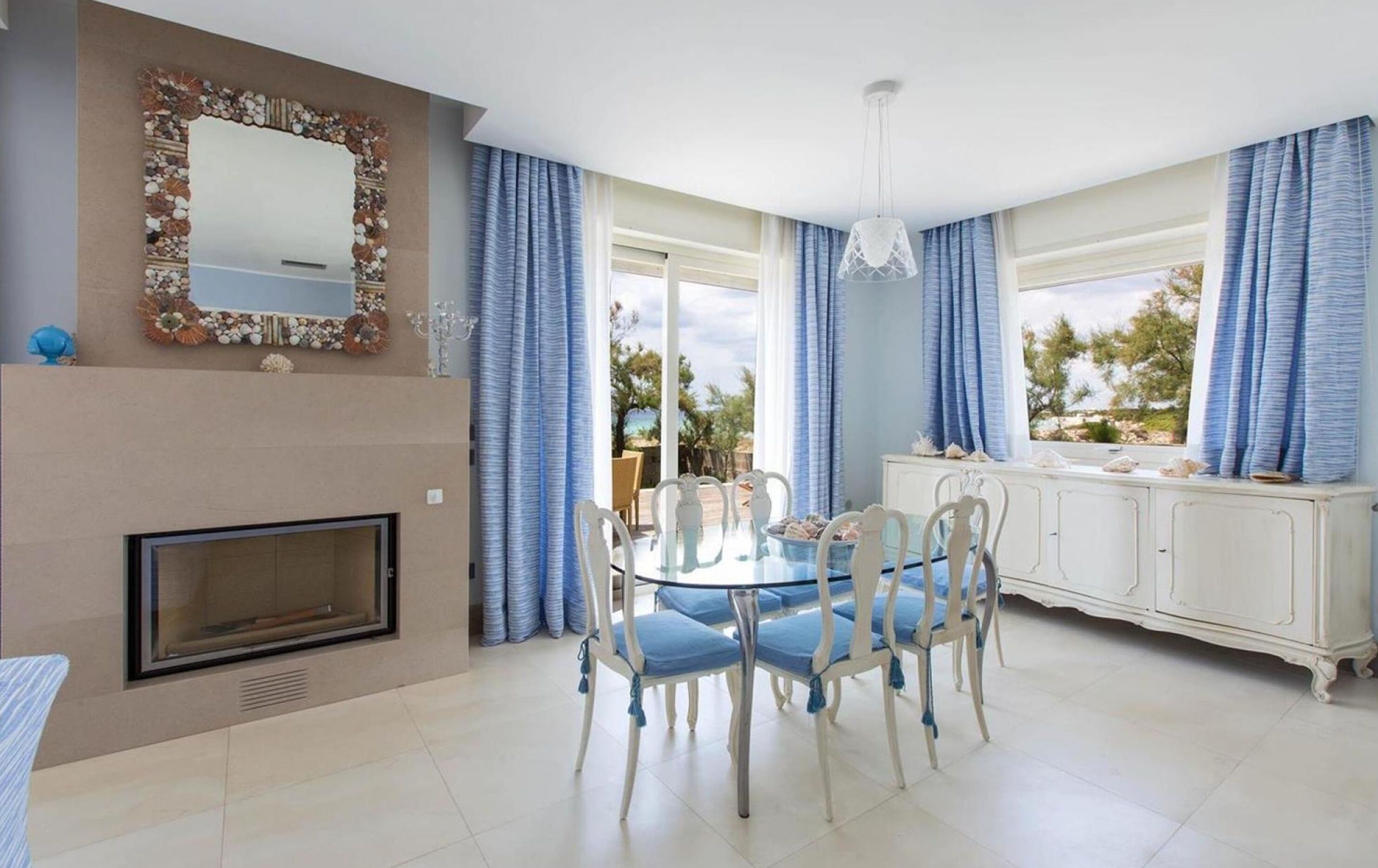 A dining area with a round table and chairs, a fireplace, a white cabinet, and a view of the outdoors.