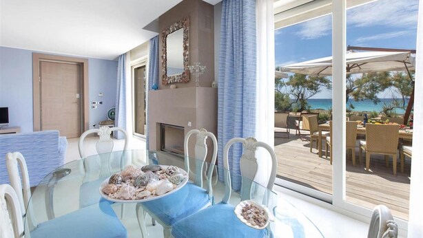 A modern room with a glass dining table, blue cushioned chairs, a fireplace, and a view of the sea. - 481 Villa di Lusso Sulla Spiaggia a Porto Cesareo (Porto Cesareo)