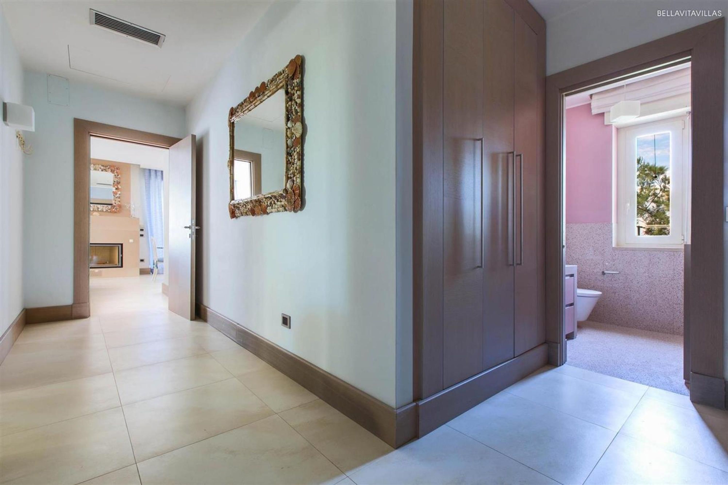 A hallway with a mirror, cabinets, and a view into a bathroom.
