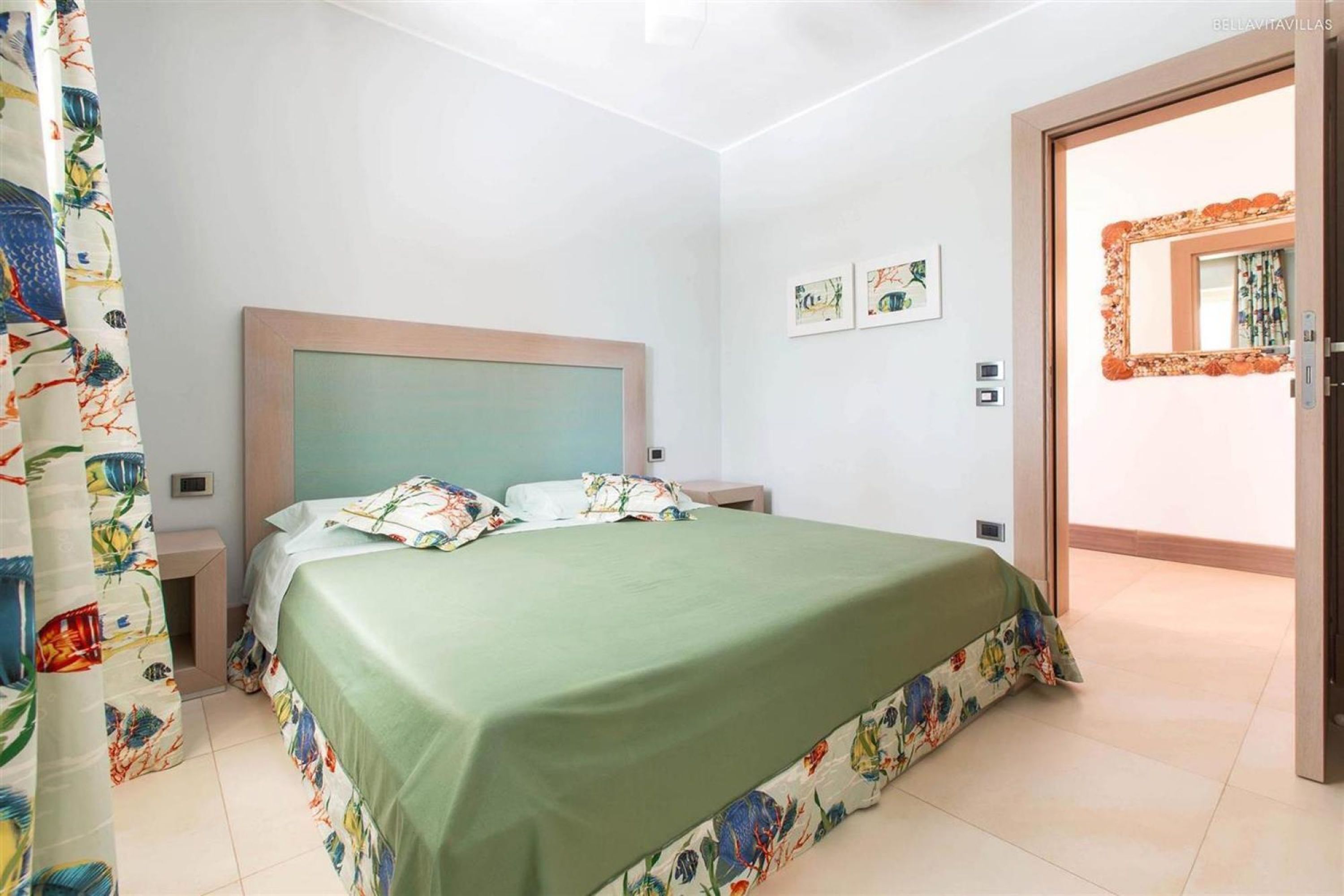Een slaapkamer met een bed, een nachtkastje, een deur en een muur met twee foto’s.