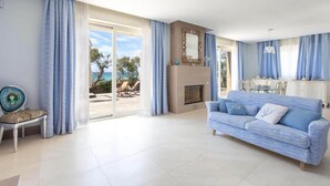 A living room with a sofa, a fireplace, and a view of the sea through large windows. - 481 Villa di Lusso Sulla Spiaggia a Porto Cesareo (Porto Cesareo)
