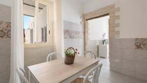 A dining area with a wooden table, white chairs, and a wicker basket with flowers. - 1643 Tenuta Fioravante - Bilo Nettuno (Porto Cesareo)