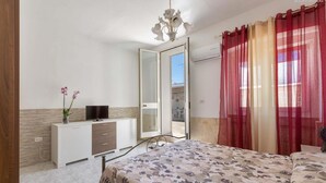 A bedroom with a bed, a TV, a dresser, a mirror, and a door leading to a balcony. - 1643 Tenuta Fioravante - Bilo Nettuno (Porto Cesareo)