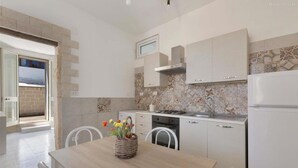 A kitchen with white cabinets, a tiled backsplash, and a dining area with a table and chairs. - 1643 Tenuta Fioravante - Bilo Nettuno (Porto Cesareo)