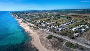 An aerial view of a coastal residential area with houses along the beach, a main road, and clear blue waters. - 1687 Villa Blu Cobalto - Appartamento 1 (Manduria)