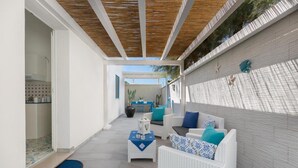 A covered outdoor area with white wicker furniture, a small table with a blue tablecloth, and a potted plant. - 1687 Villa Blu Cobalto - Appartamento 1 (Manduria)