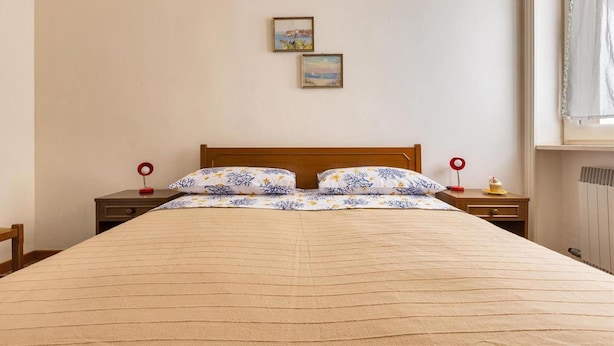 Una cama bien hecha con un edredón floral, dos mesitas de noche con lámparas rojas y dos cuadros en la pared.