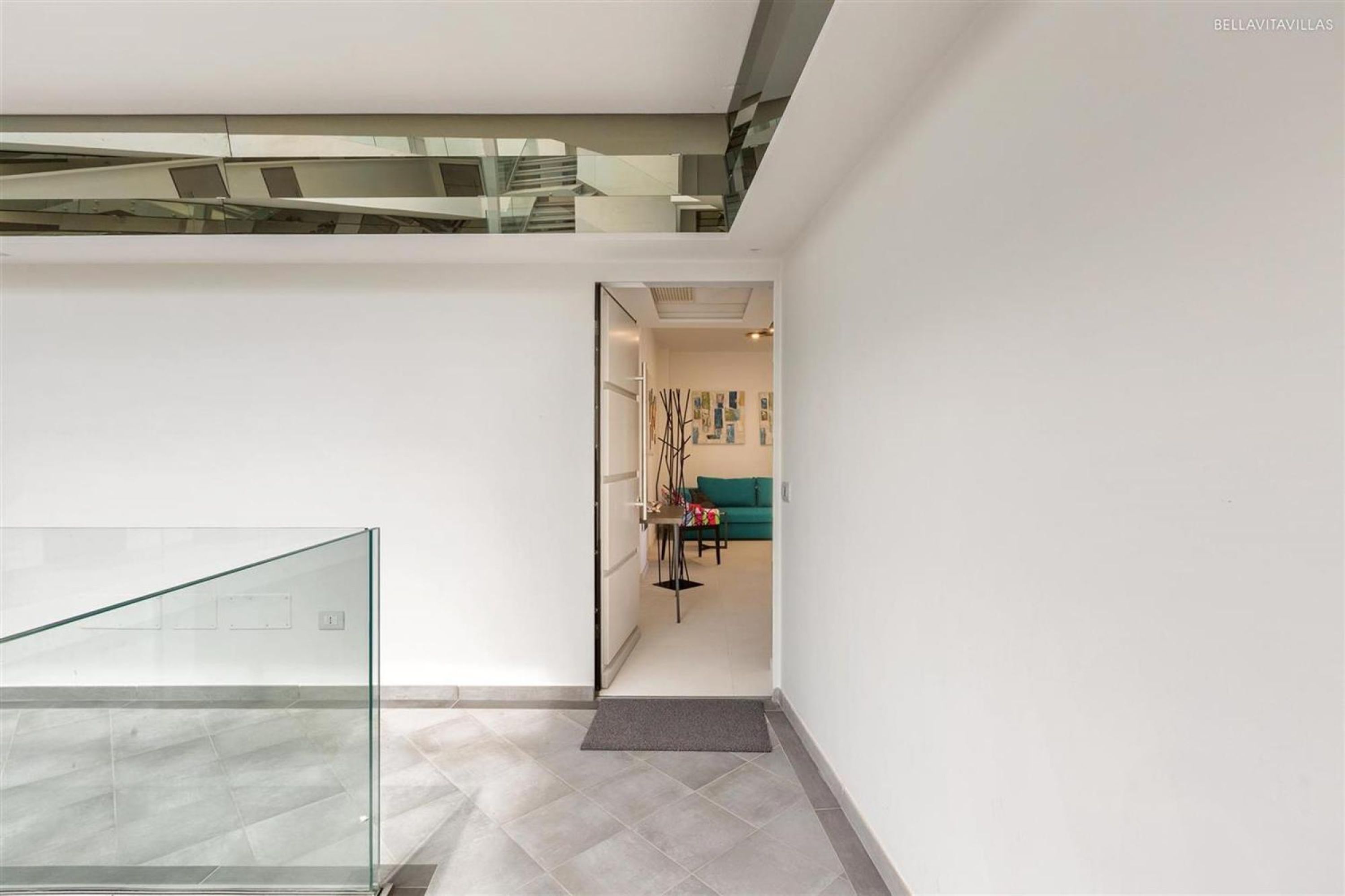 A modern interior with a glass railing, a staircase, and a living area with artwork and a sofa.