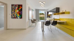 A modern kitchen with yellow cabinets, a dining area with chairs, and a colorful abstract painting on the wall. - 1937 Bella Vita Appartamento Simone (Gallipoli)