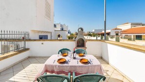En balkon med et bord dækket til to, en grill og udsigt over bybilledet.