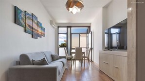 Ein modernes Wohnzimmer mit grauem Sofa, einem Essbereich mit Tisch und Stühlen, einer Küche mit Schränken und einem großen Fernseher.