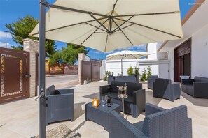 Eine Terrasse im Freien mit Korbmöbeln, einem Tisch mit Flasche und Gläsern sowie einem großen Sonnenschirm.